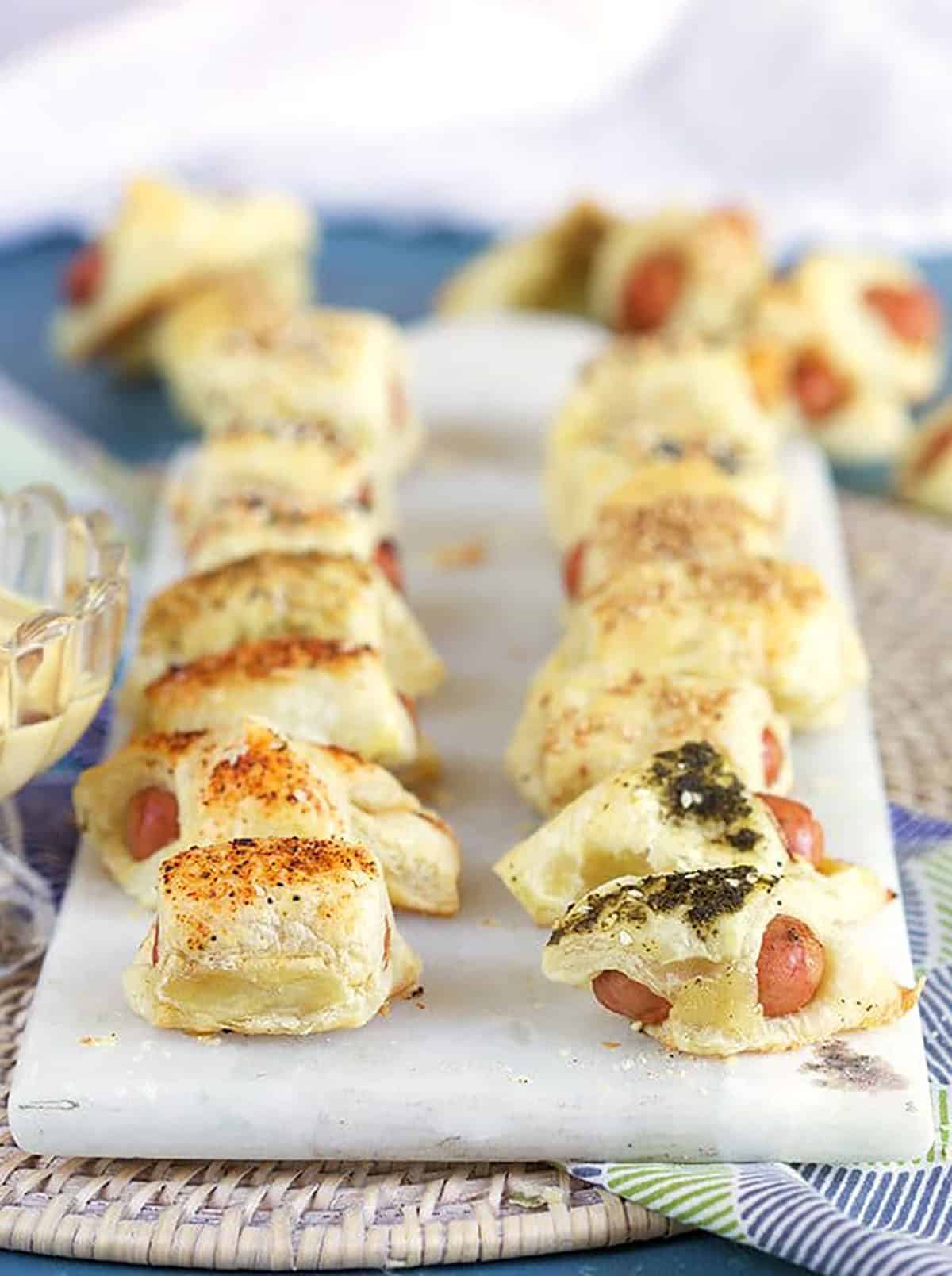 Pigs in a Blanket arranged in two rows on a white marble board.