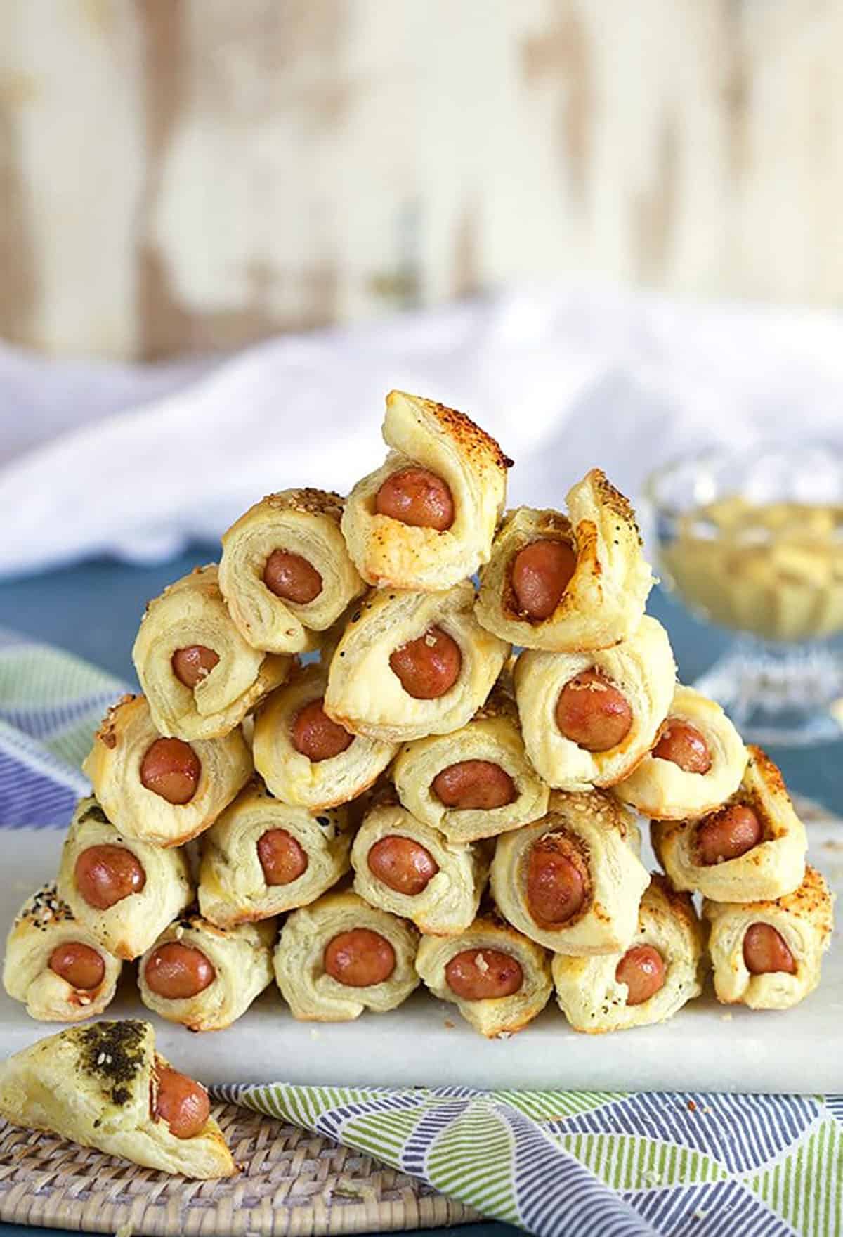 Pigs in a blanket piled in a pyrimad form on a marble tray.
