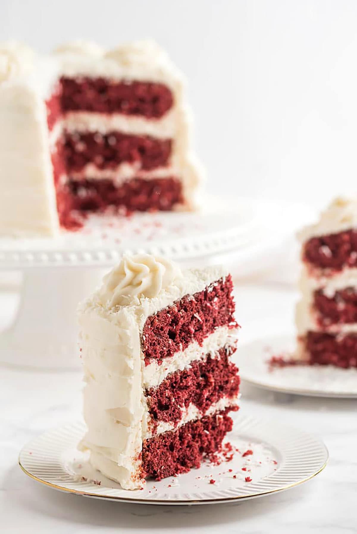 slice of red velvet coconut cake on a white plate with the whole cake in the background.