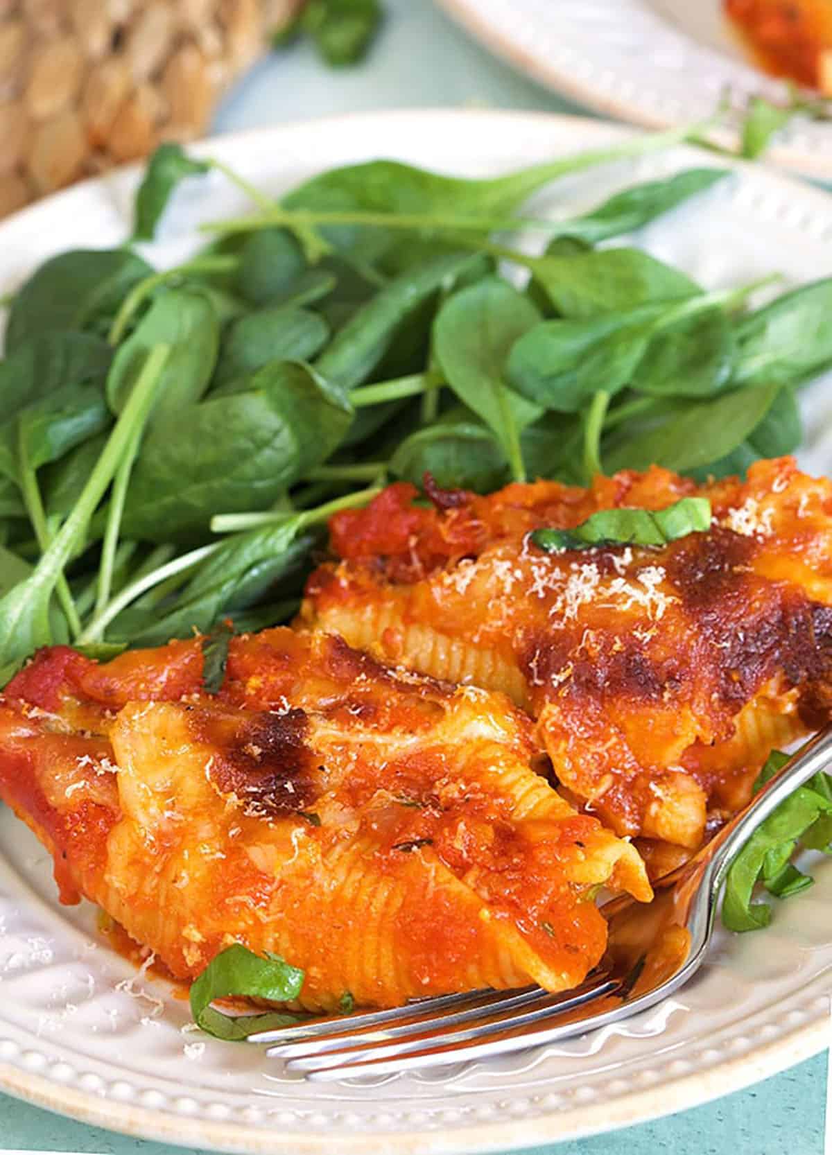 A serving of stuffed shells is on a white plate, next to a helping of spinach leaves.