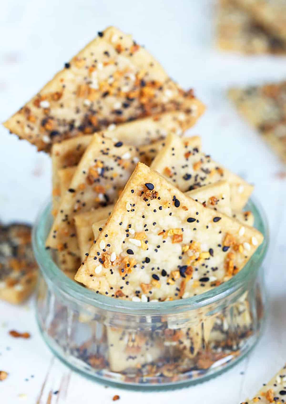 Several homemade crackers are placed in a tiny glass cup on a white surface.