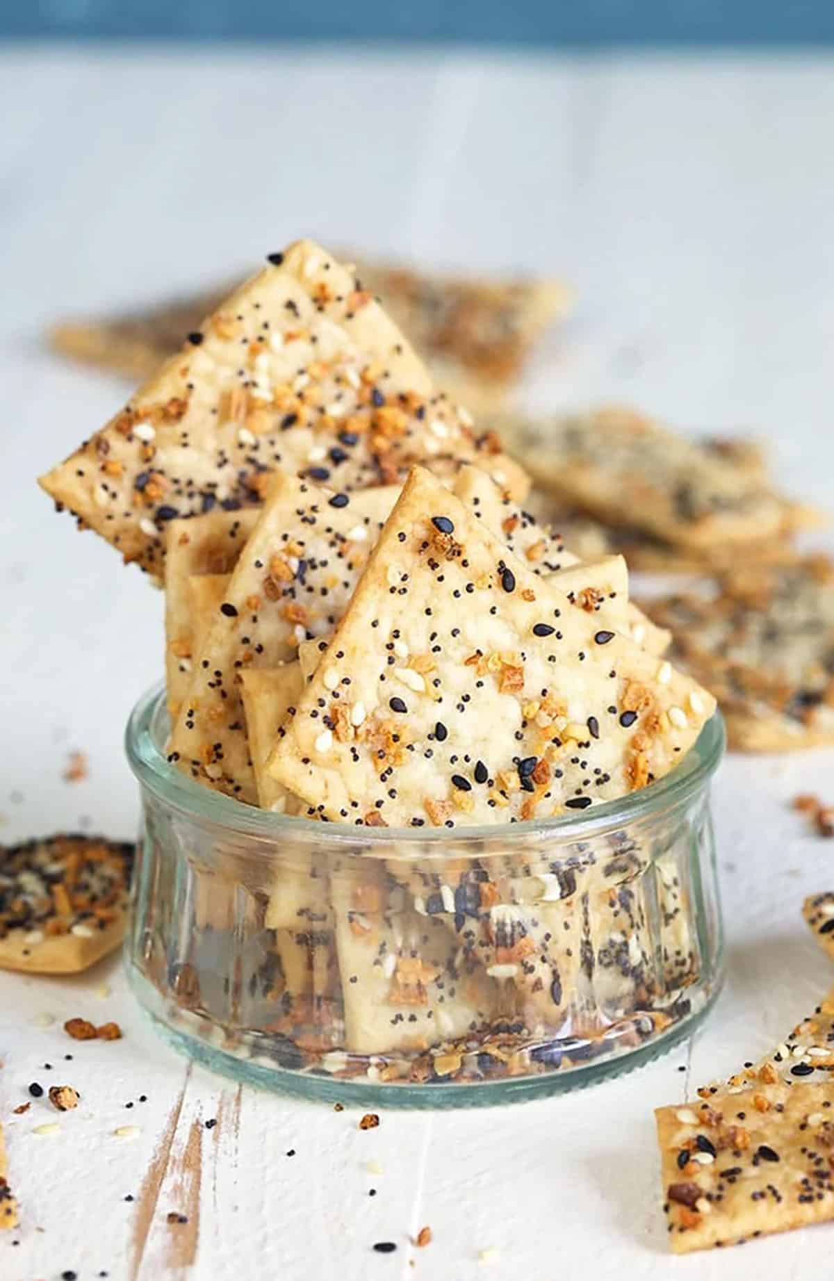 A few everything crackers are placed in a small glass cup on a white surface. 