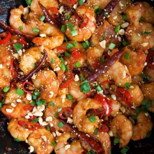 Shrimps are coated with Szechuan sauce in a large black skillet.