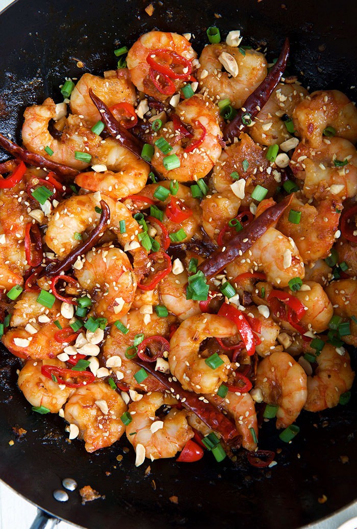 Shrimps are coated with Szechuan sauce in a large black skillet.