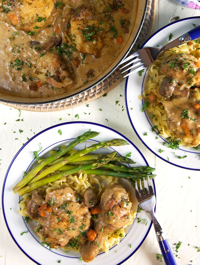 A plate of chicken fricassee sits next to a large, full dutch oven.