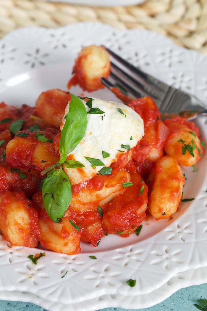 A single gnocchi is on a fork, while the rest of the entree remains on a white plate.