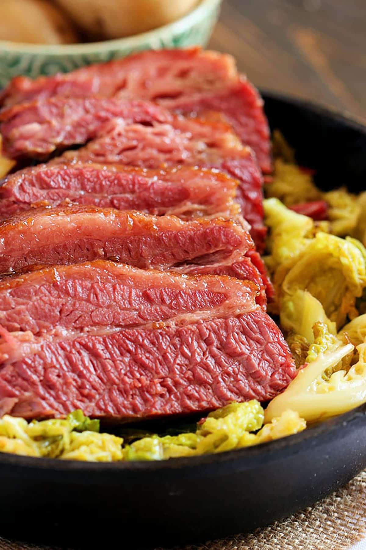 Corned beef sliced and arranged on a pile of sautéed cabbage in a cast iron skillet