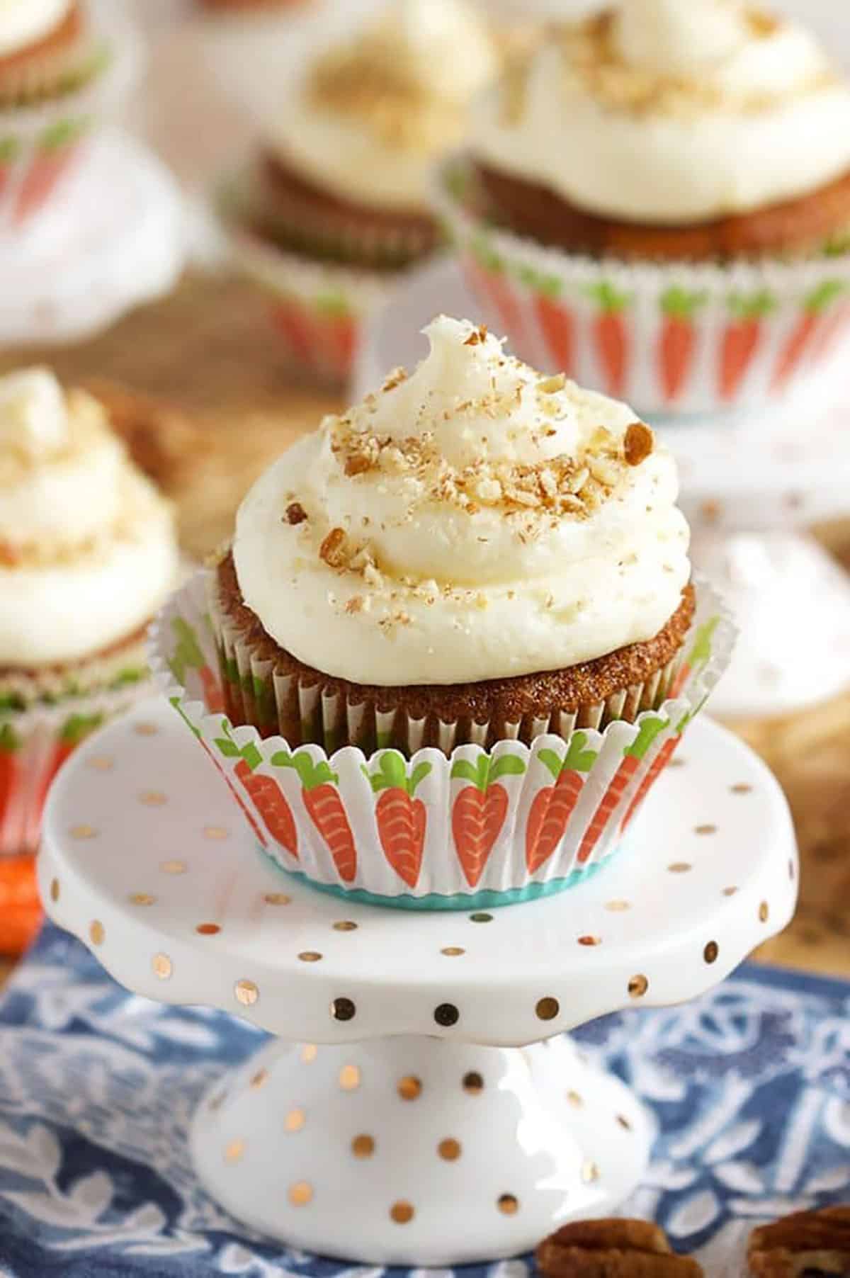 Carrot Cake Cupcake topped with cream cheese frosting and sprinkled with crushed pecans on a cupcake stand.