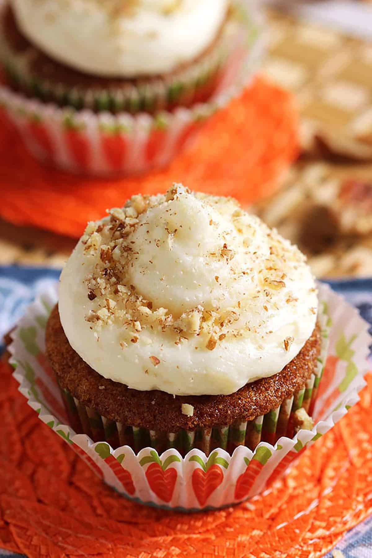 Carrot Cake Cupcake with cream cheese frosting in a cupcake wrapper on an orange coaster.