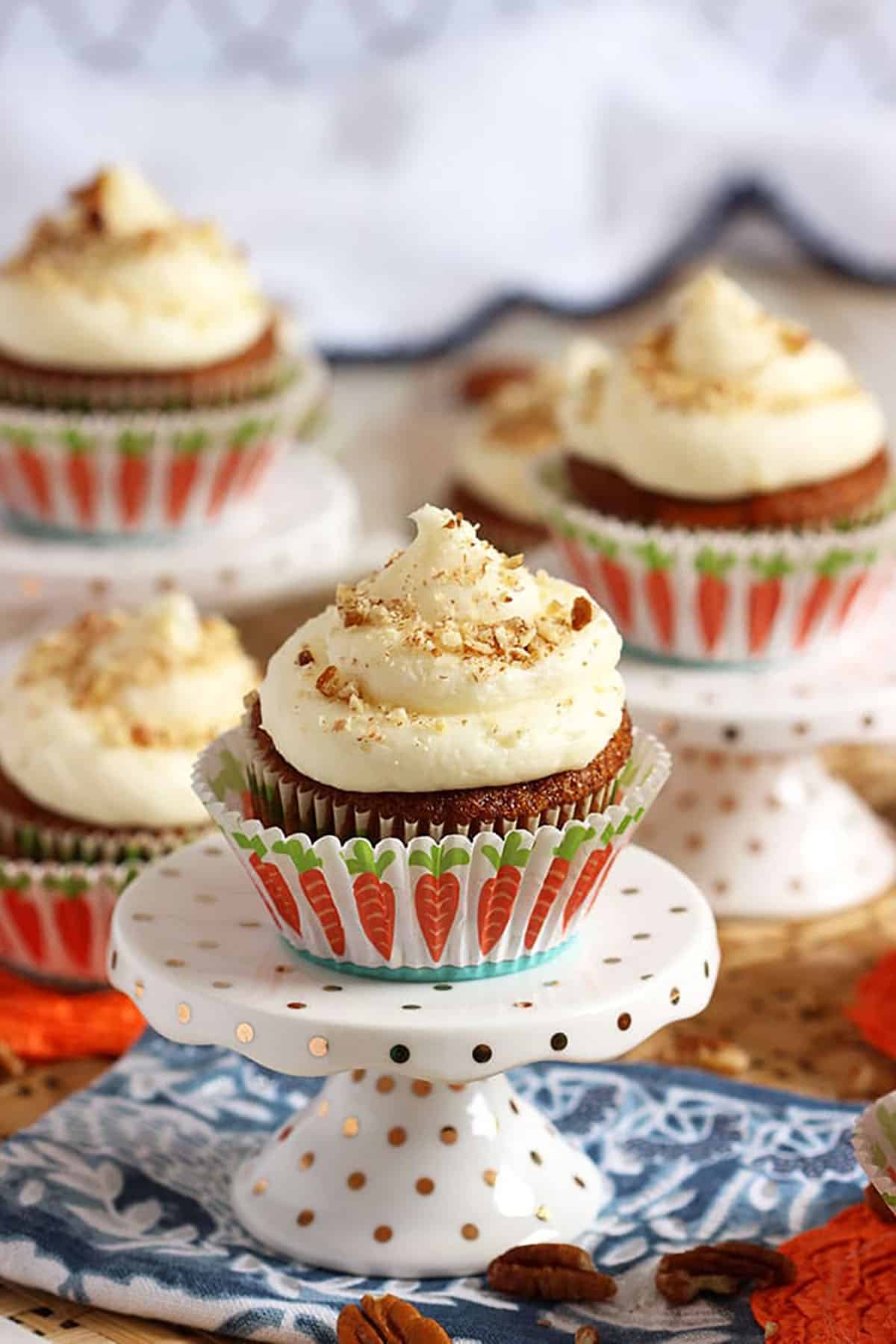 Carrot Cake Cupcake on a white cupcake stand in a cupcake wrapper with carrots on it.