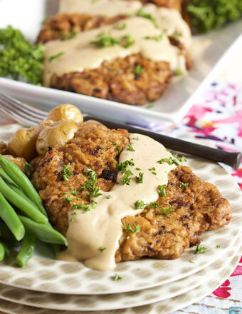 Chicken Fried Steak on a white plate with gravy on top and a side of green beans.