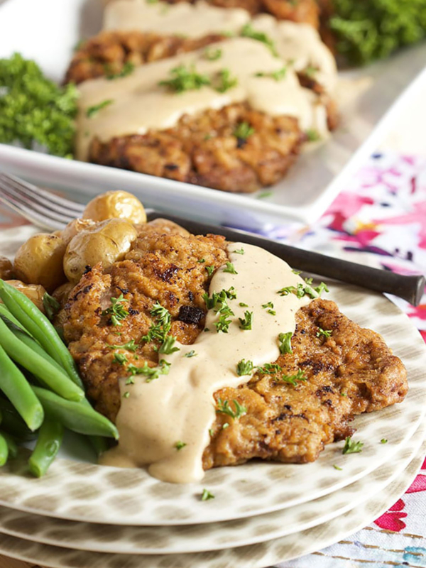 Chicken Fried Steak on a white plate with gravy on top and a side of green beans.