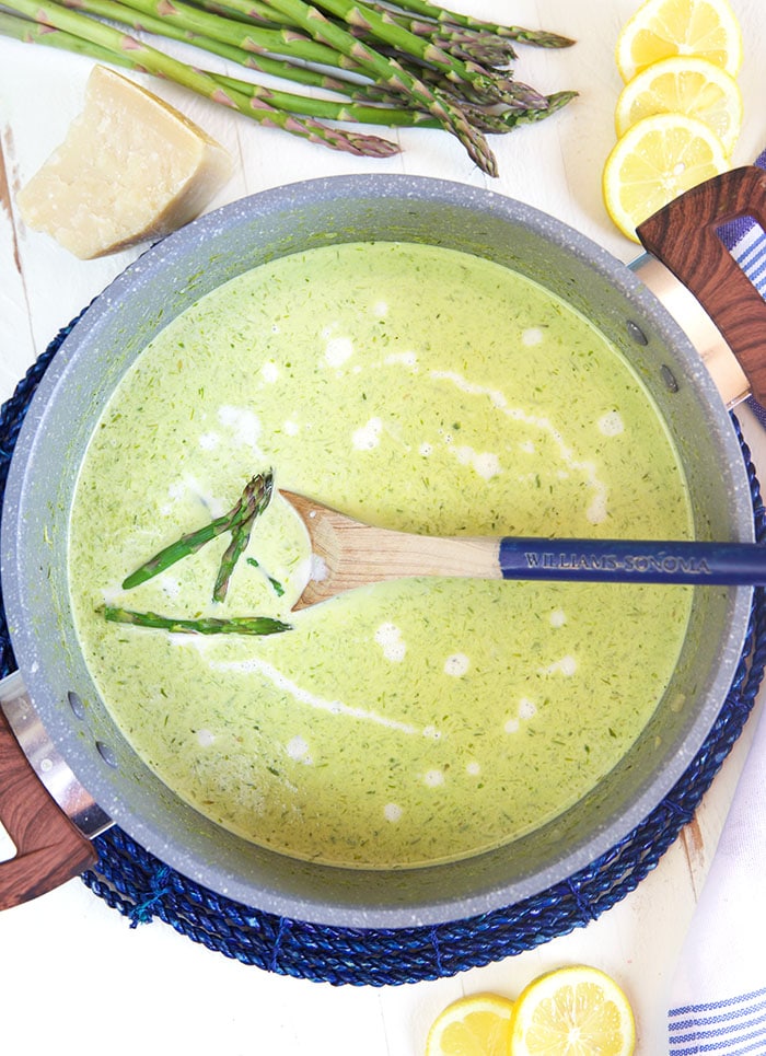 A large spoon is mixing a pot of cream of asparagus soup.