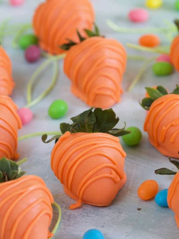 Orange drizzled strawberries are placed on a white surface.