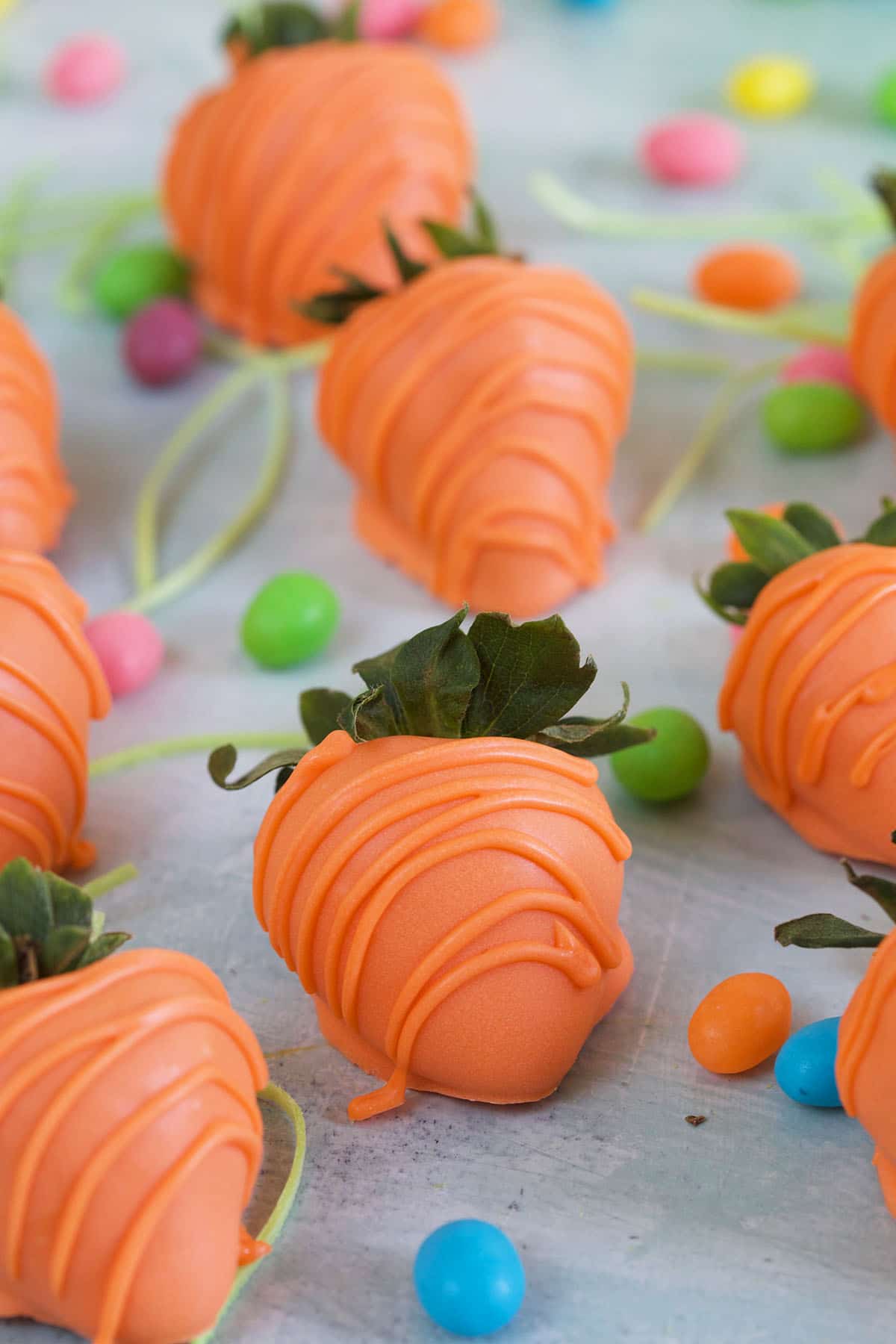 Orange drizzled strawberries are placed on a white surface. 