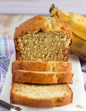 Banana Bread sliced on a marble board with bananas in the background.