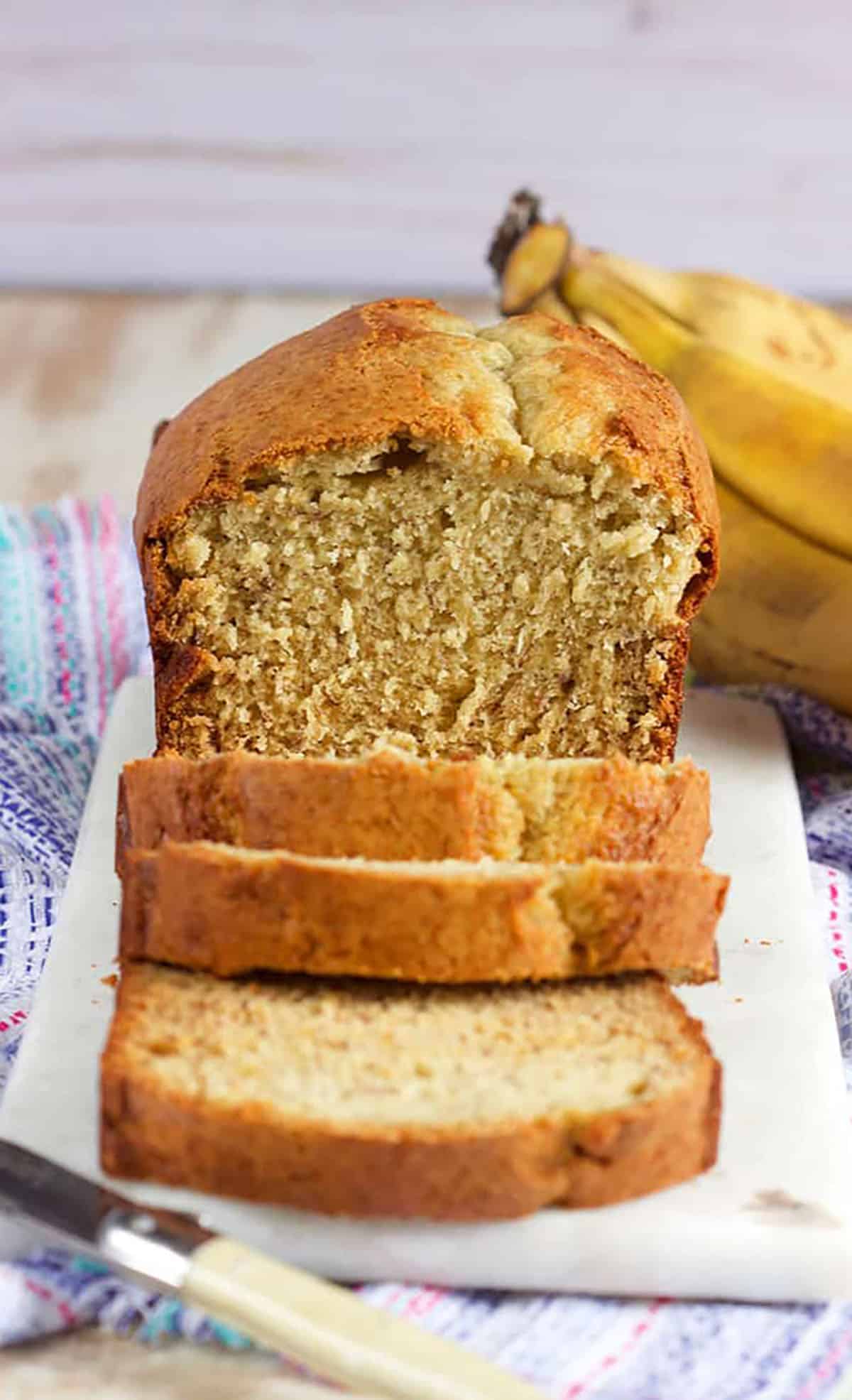 Banana Bread sliced on a marble board with bananas in the background.