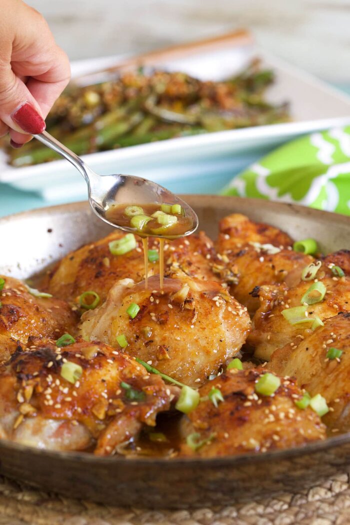 A spoon is drizzling honey garlic sauce over chicken thighs.