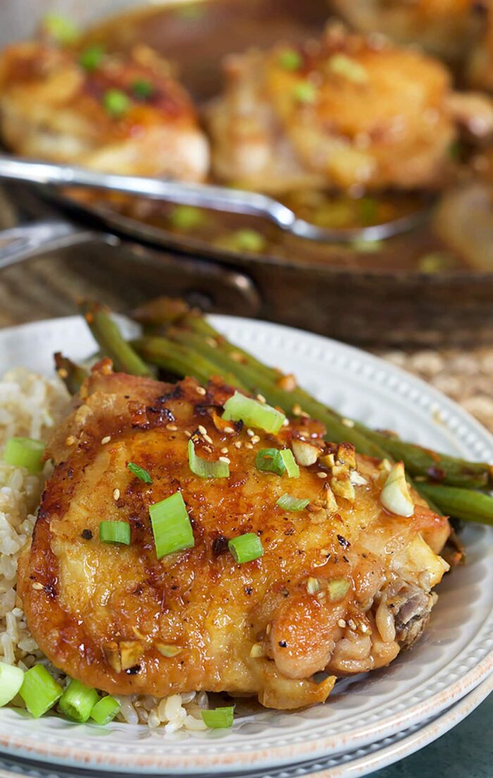 A honey garlic thigh is on a white plate, next to asparagus and rice.
