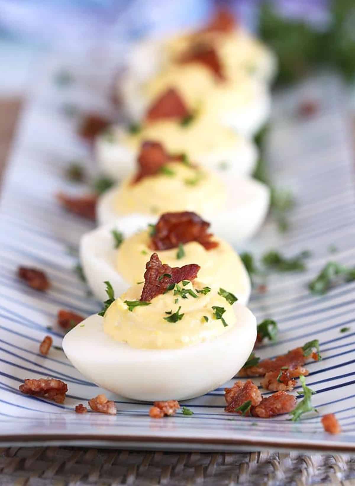 Bacon Horseradish Deviled Eggs in a row on a blue and white striped platter.