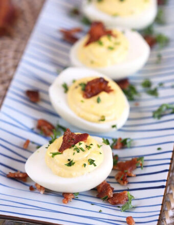 Overhead shot of bacon horseradish deviled eggs on a blue and white striped platter.