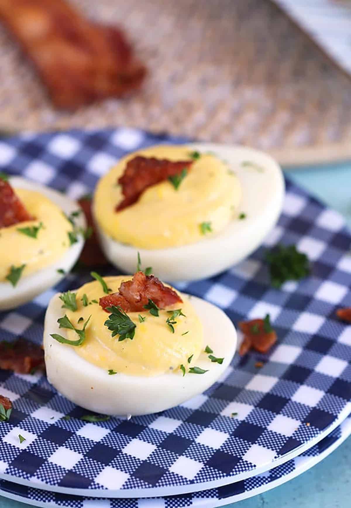 Bacon Horseradish Deviled Eggs on a blue and white gingham plate with bacon in the background.