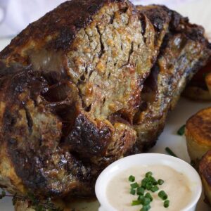 A fully cooked prime rib roast is placed next to a small cup of horseradish.