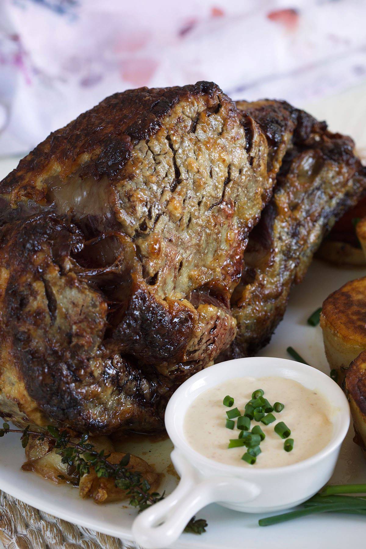 A fully cooked prime rib roast is placed next to a small cup of horseradish. 