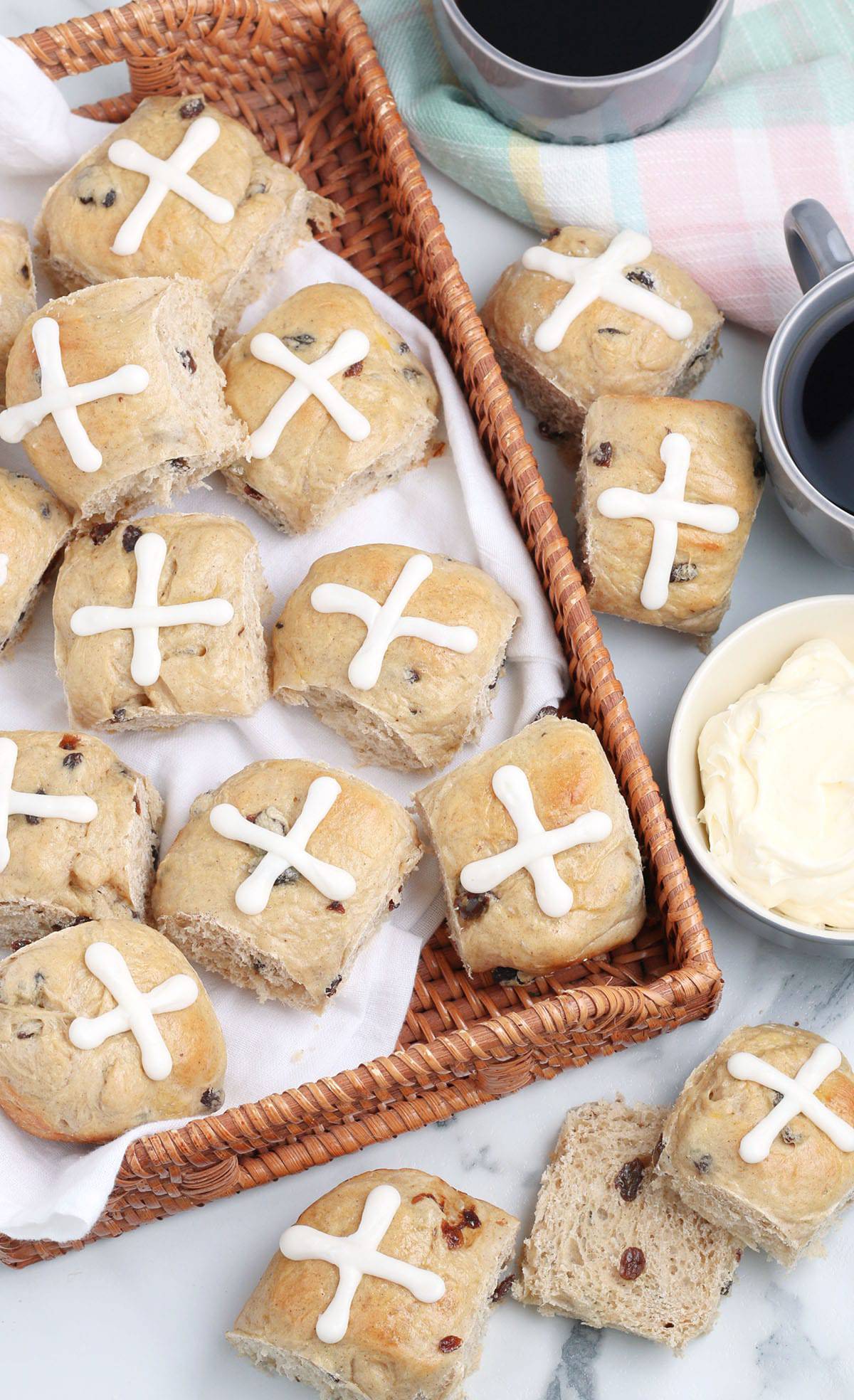 Hot Cross buns in a wicker tray with a bowl of frosting and two mugs of coffee.