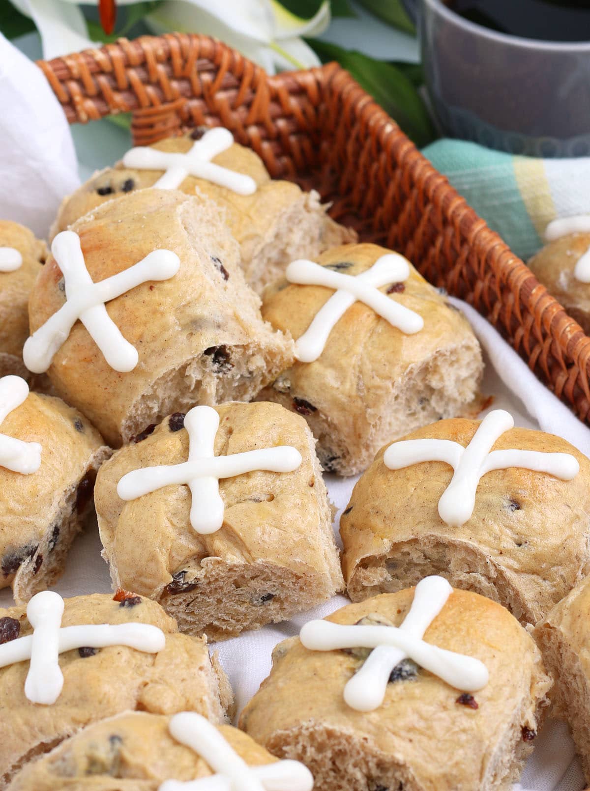 Hot Cross buns in a wicker tray with a cup of coffee in the background.