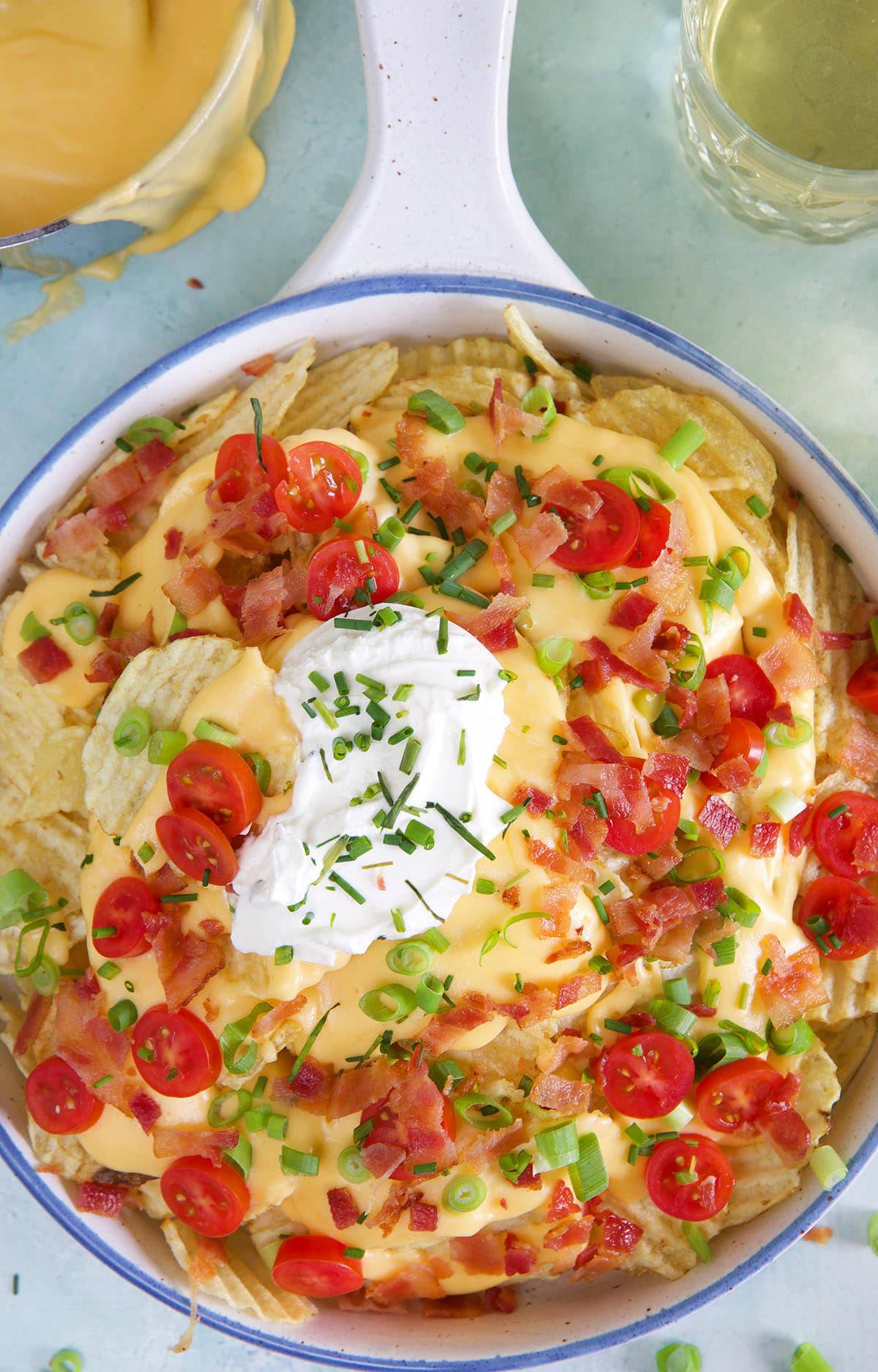 Sour cream, chives, tomatoes and green onions are sprinkled on a serving of beer cheese nachos.