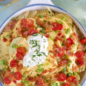 A large white bowl of Irish nachos is garnished with tomatoes and green onions.