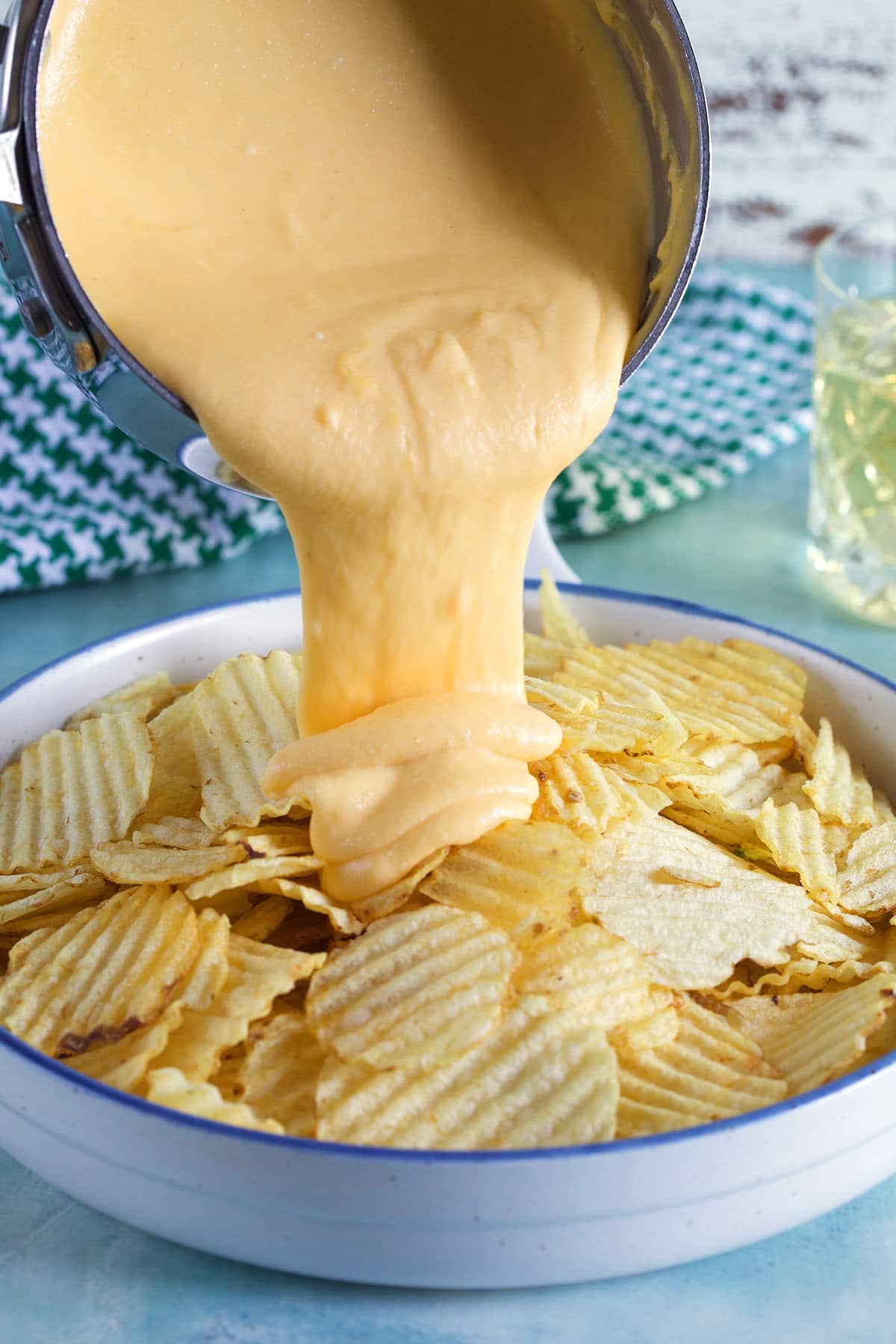 Beer cheese sauce is being poured on to potato chips.