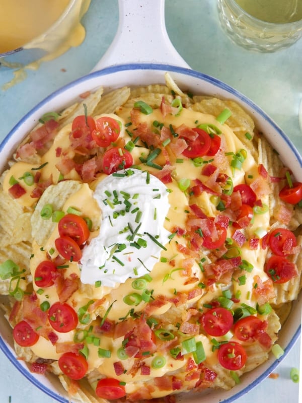 A large white bowl of Irish nachos is garnished with tomatoes and green onions.