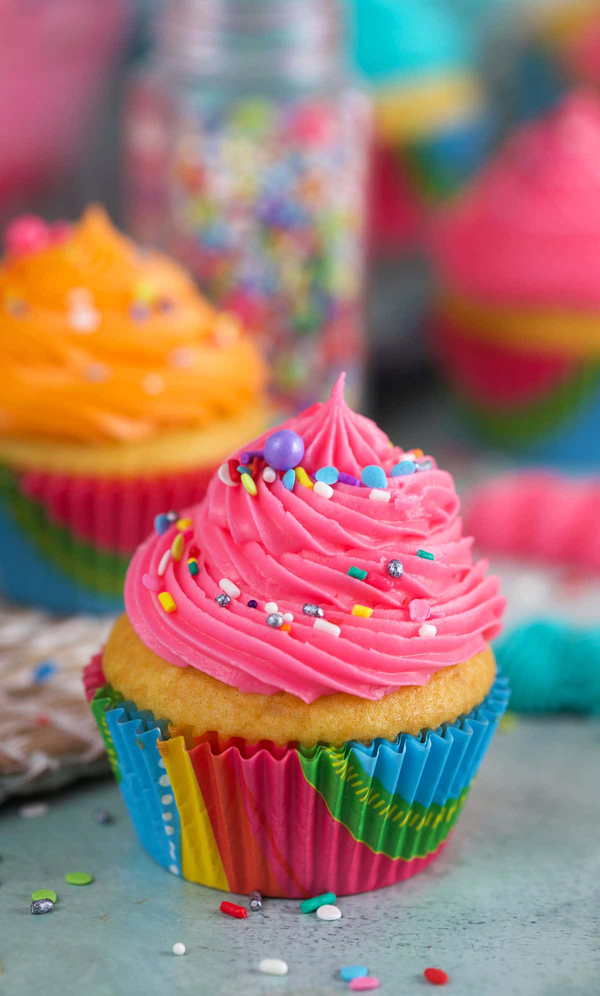 A pink cupcake is sprinkled with rainbow sprinkles. 