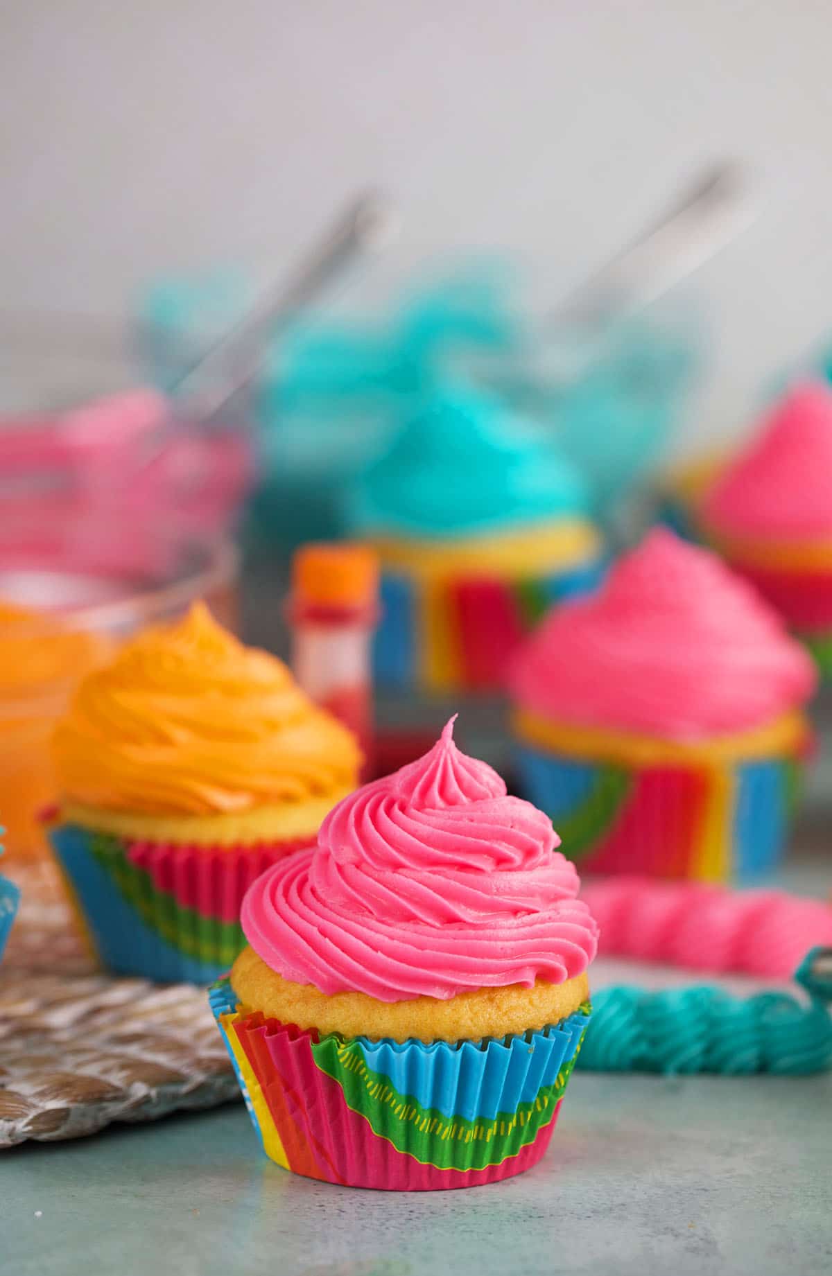 Pink, blue, and orange frosted cupcakes are presented on a countertop.