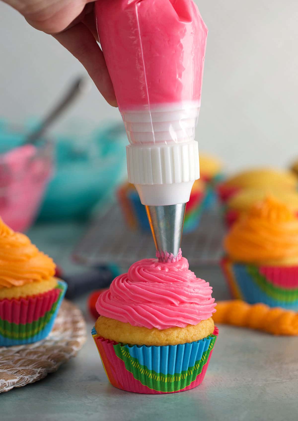A piping bag is piping pink frosting onto a vanilla cupcake.