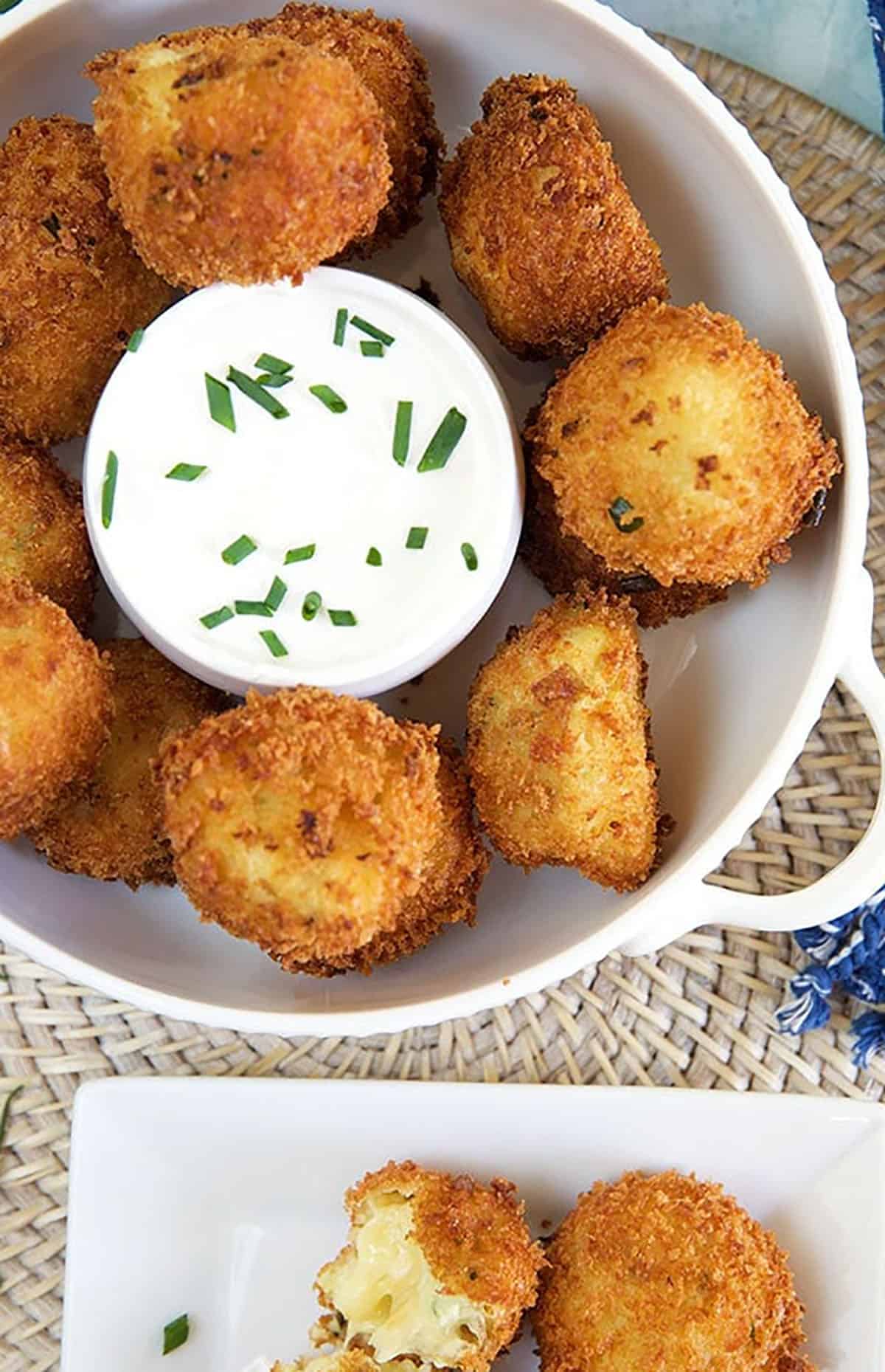 A bowl full of croquettes sits next to a plate with several croquettes.