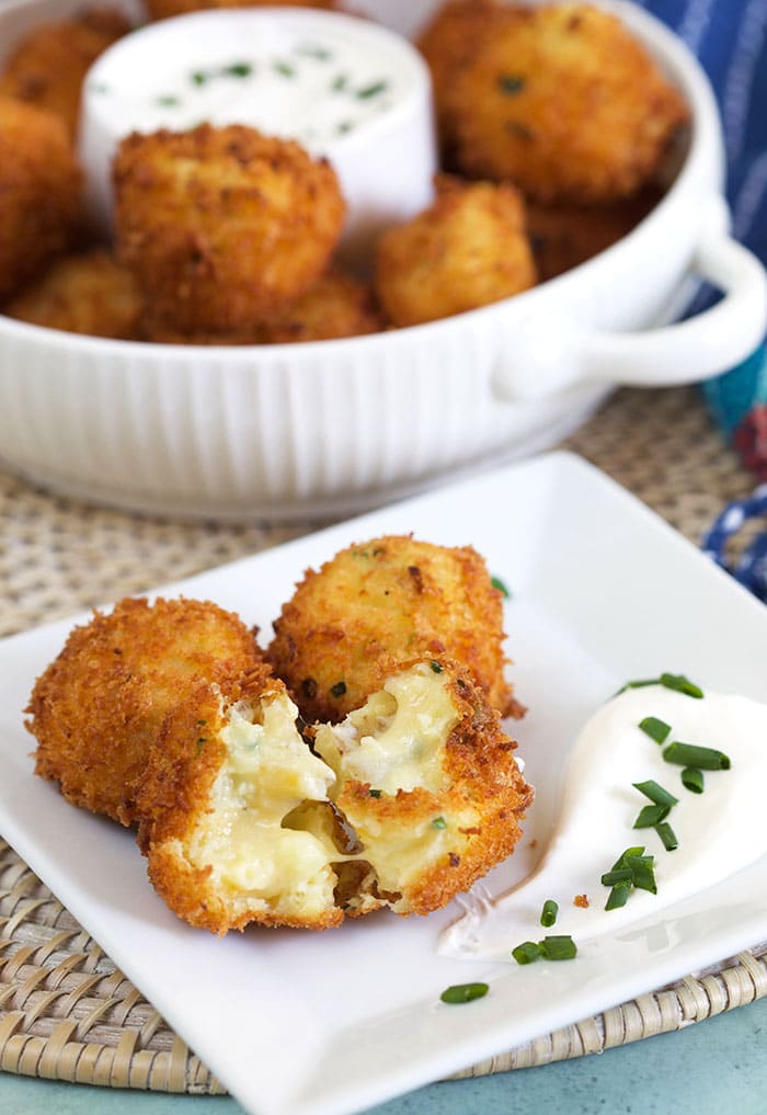 Croquettes are on a white plate with a bit of sour cream and chives on the side.
