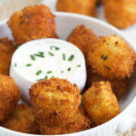A bowl of potato croquettes is presented with a bowl of sour cream in the middle.