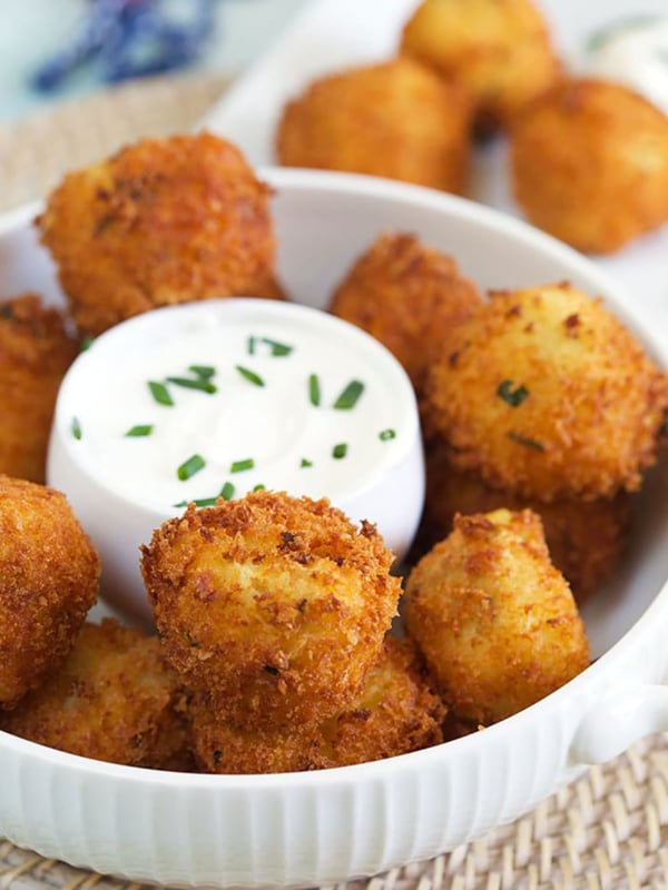A bowl of potato croquettes is presented with a bowl of sour cream in the middle.