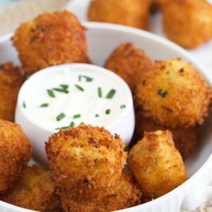 A bowl of potato croquettes is presented with a bowl of sour cream in the middle.