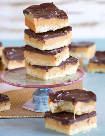 Millionaire shortbread bars stacked on a mini cakeplate on a blue background.