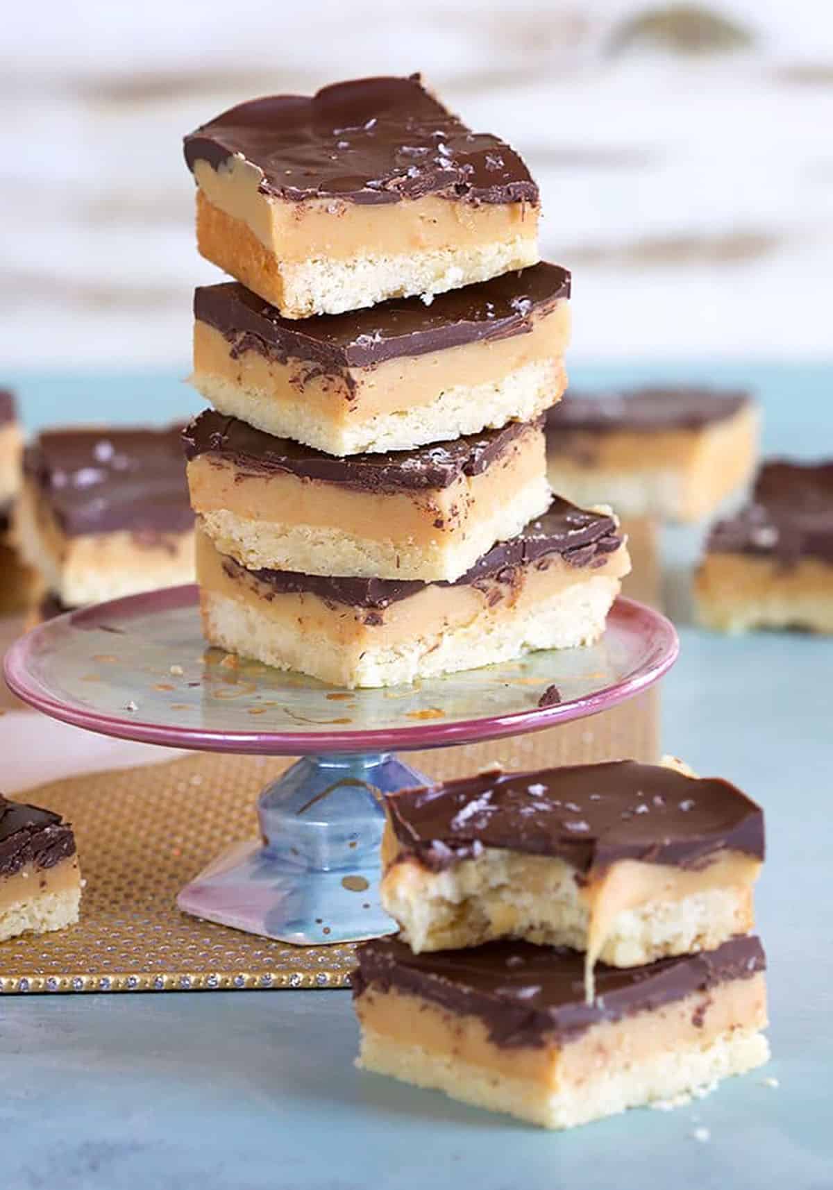 Millionaire shortbread bars stacked on a mini cakeplate on a blue background.