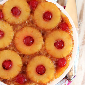 Pineapple Upside Down Cake on a white cake plate on a distressed white wood backdrop.