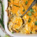 A large serving spoon is dipping into a casserole dish filled with cheesy potatoes.