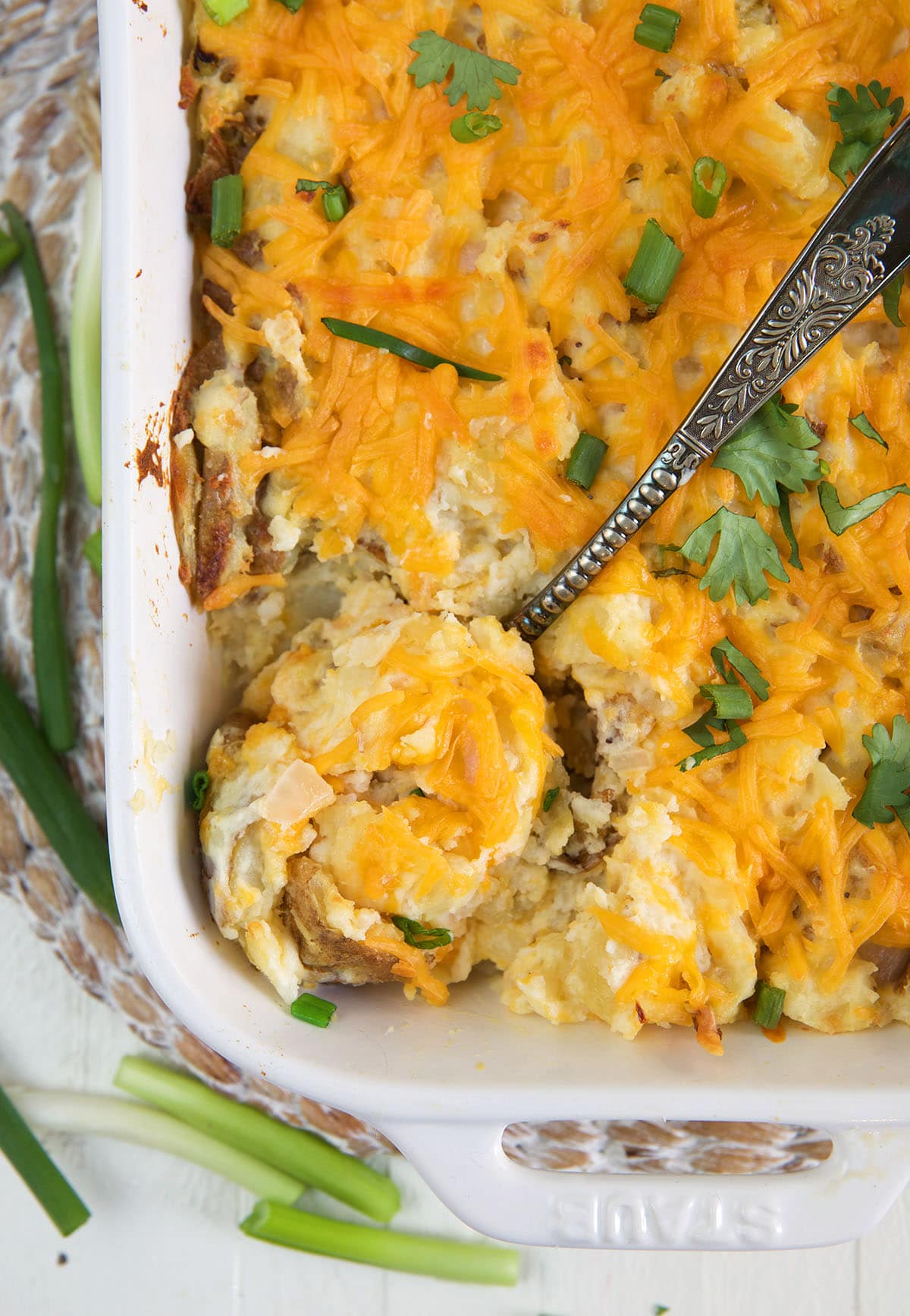A large serving spoon is dipping into a casserole dish filled with cheesy potatoes.
