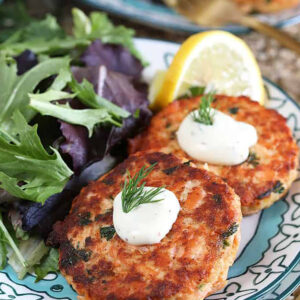 Two salmon cakes with lemon dill sauce on a decorative blue and white plate with a gold fork