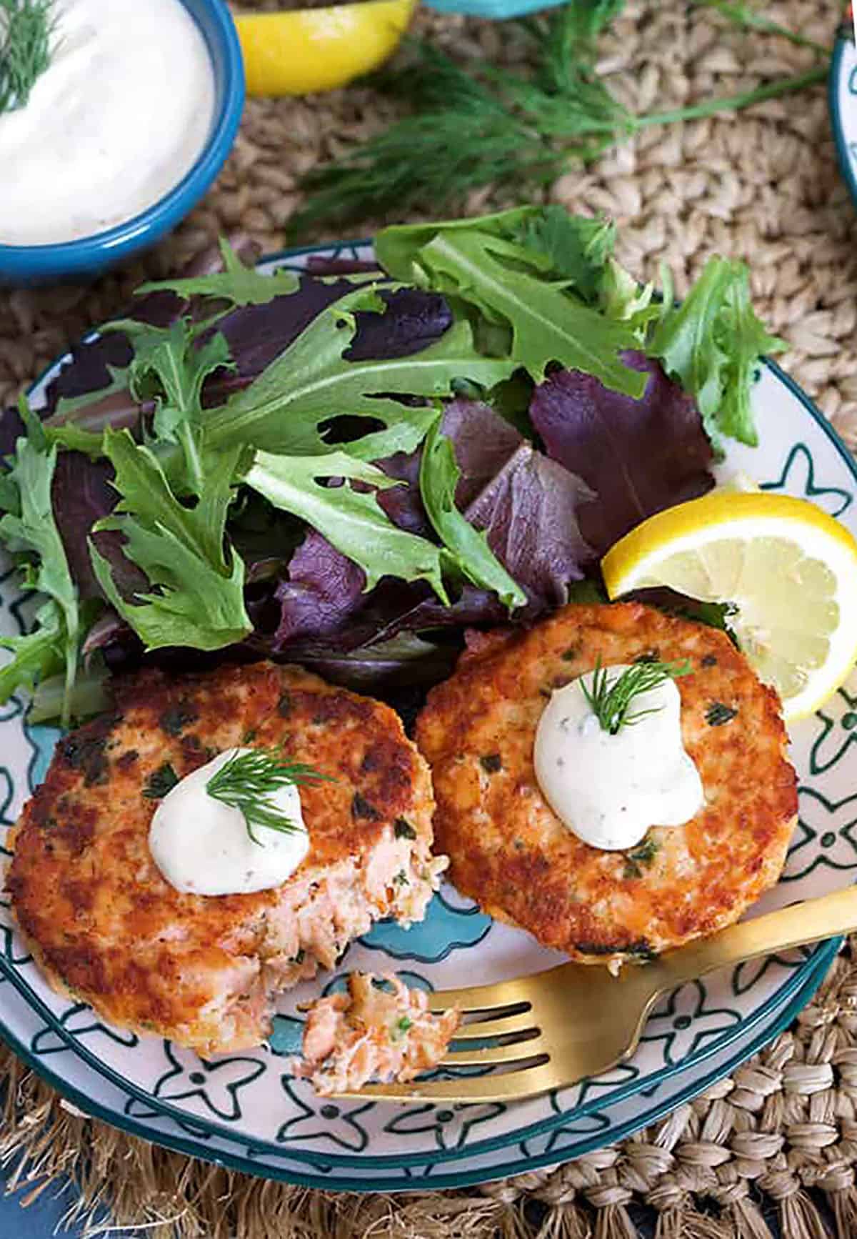 Overhead shot of Salmon Cakes Recipe with Lemon Dill Sauce on blue and white plate with sauce in a blue bowl 