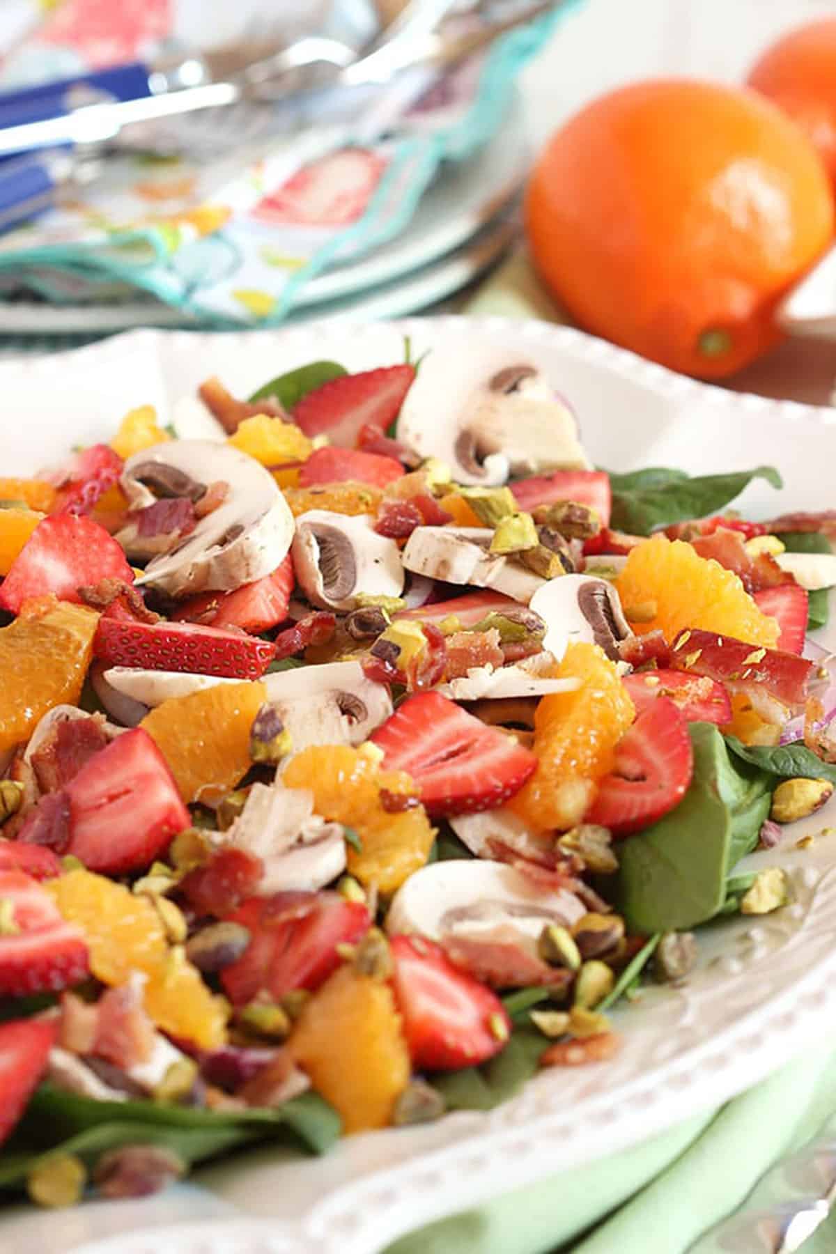 Strawberry Spinach Salad on a white platter with oranges and bacon.